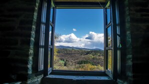 Uma janela aberta com vista para uma paisagem arborizada e montanhas ao longe.