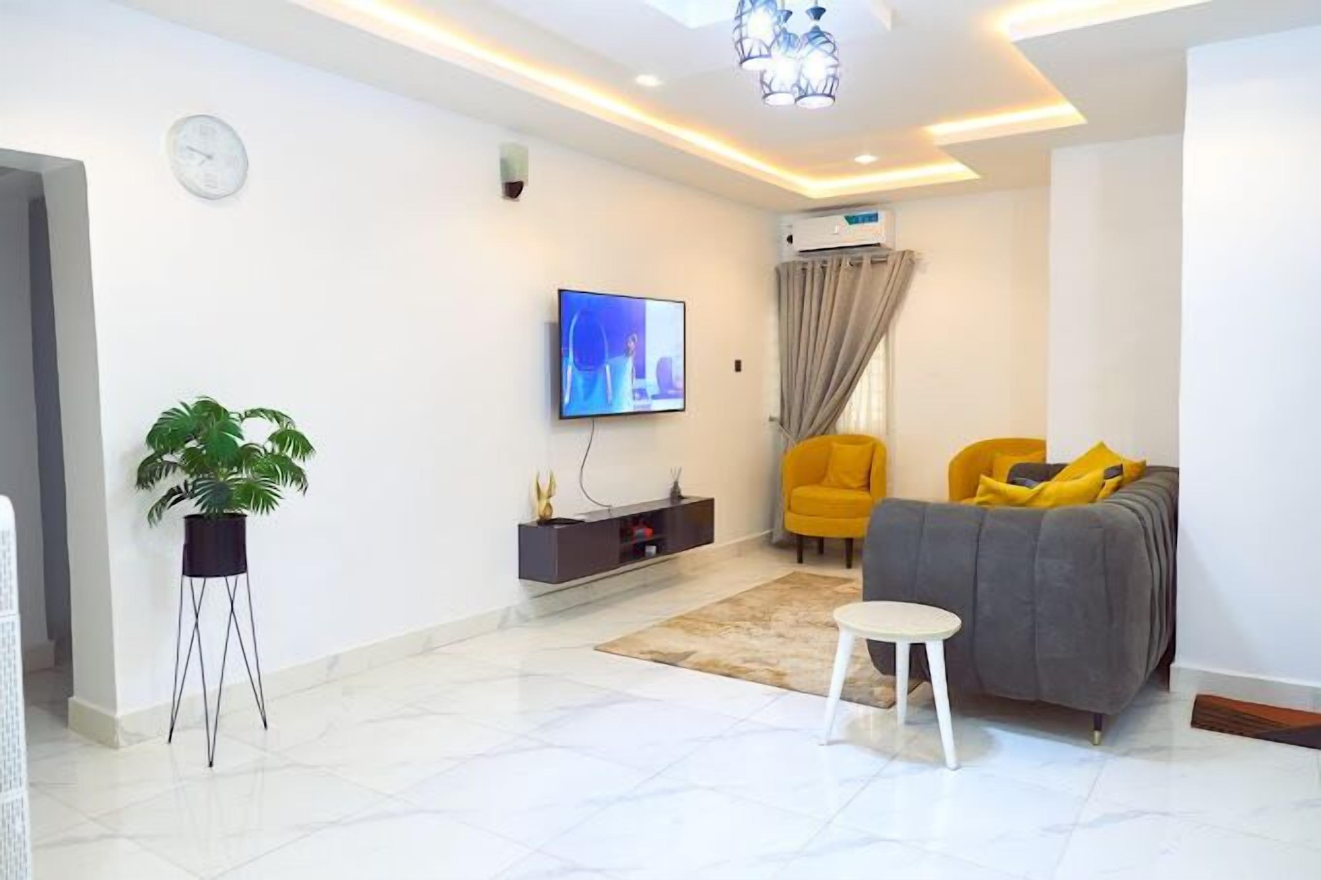 A modern living room with a flat-screen TV, a sofa, a chair, and a small table.