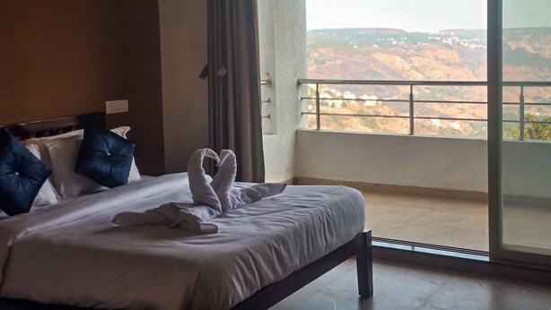Camera d'hotel con un letto, cuscini e vista su un paesaggio montano dal balcone.