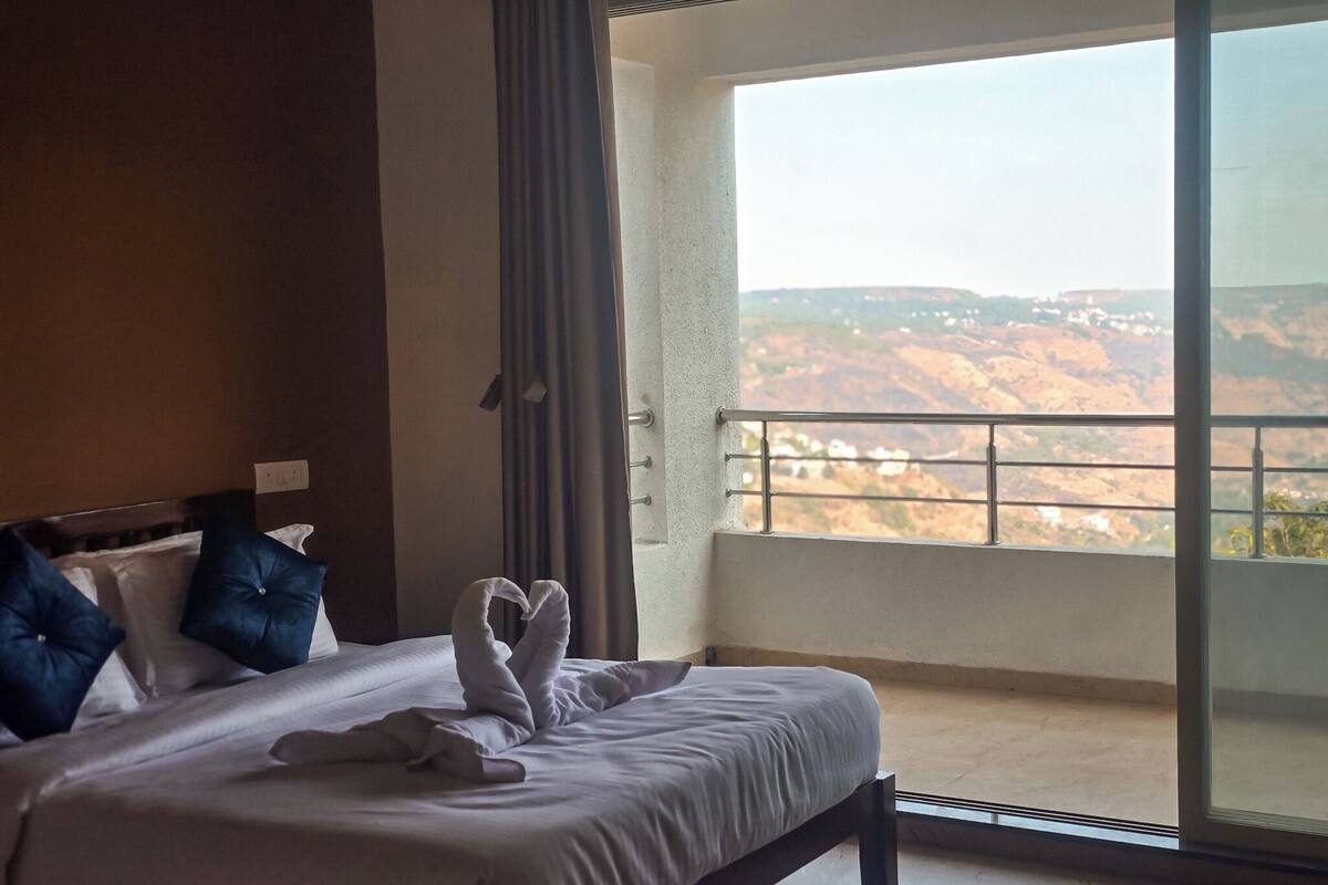 Ein Hotelzimmer mit Bett, Kissen und Blick auf eine gebirgige Landschaft vom Balkon aus.