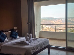 Habitación de hotel con cama, almohadas y vista a un paisaje montañoso desde un balcón.