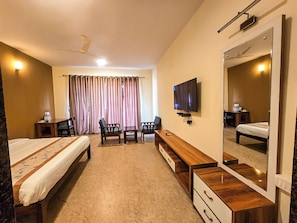 Relax in a spacious room with a large bed, desk, and seating area, featuring a flat-screen TV and a large mirror.