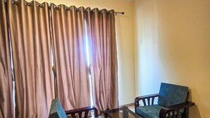 Una stanza con due sedie di legno e un tavolo in vetro, un pavimento color beige e una tenda con un lampadario sopra.