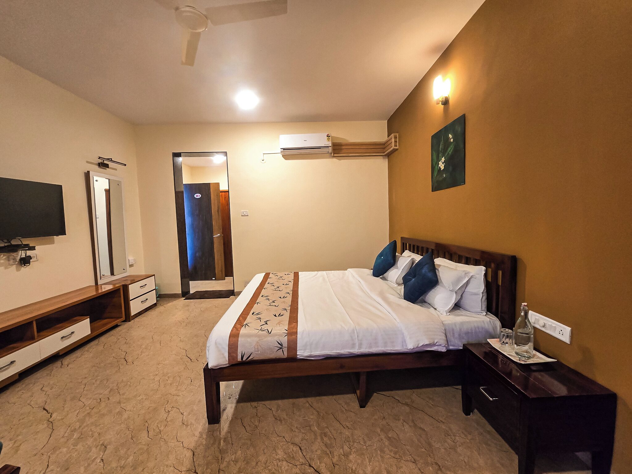 Quarto com cama, mesa de cabeceira, televisão, guarda-roupa e ar condicionado.