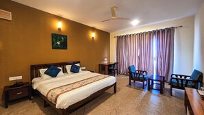 Una camera d'albergo con un letto, una scrivania, due sedie, una ventola a soffitto e una finestra con tende.