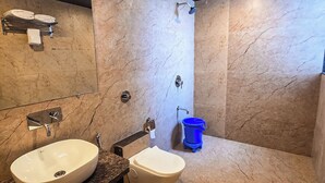 Bagno con due lavandini, uno specchio, un portascopino, una doccia e un cestino della spazzatura blu.