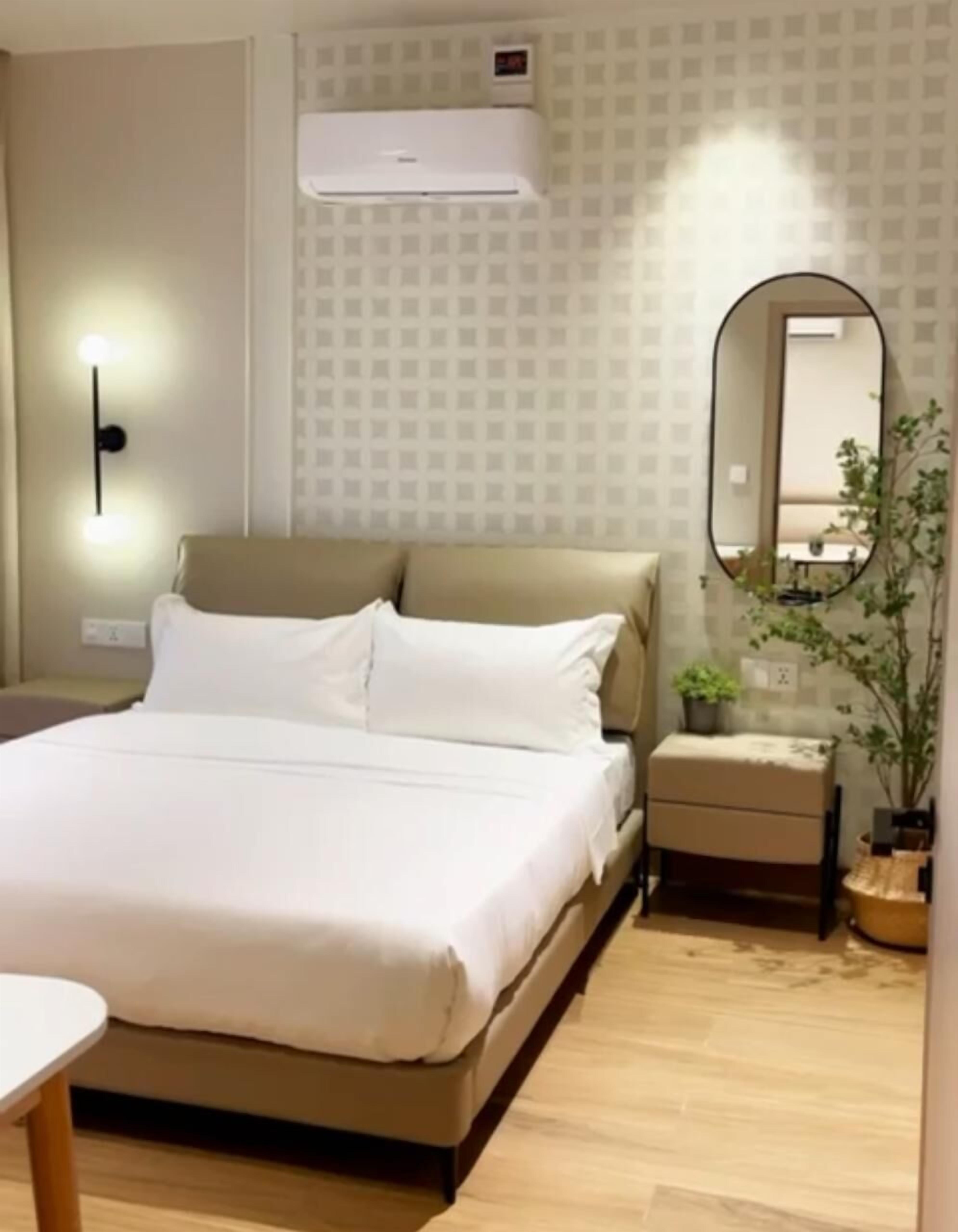 A hotel room with a bed, bedside table, nightstand, and a mirror.