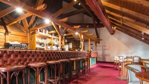 Un espace bar agrémenté de poutres en bois, d’un comptoir en cuir capitonné et de chaises en bois.