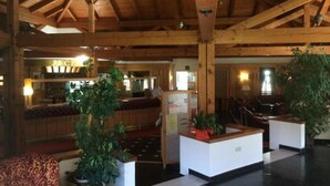 Un hall d'entrée avec des poutres en bois, un comptoir d'accueil, un espace salon et des plantes en pot.