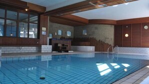 Une grande piscine intérieure aux murs carrelés et aux poutres en bois.