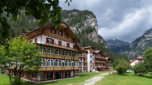 Un bâtiment de style chalet traditionnel, doté de nombreux balcons, entouré d’une végétation luxuriante et avec des montagnes en toile de fond.