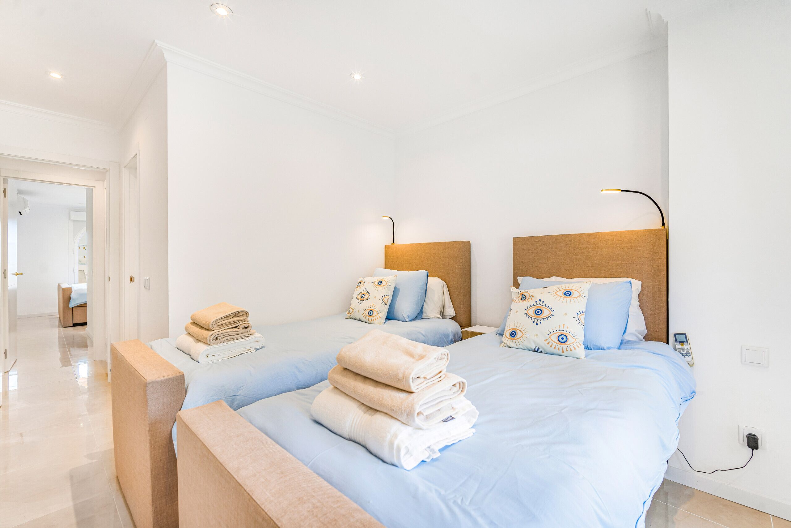 Une chambre d’hôtel avec deux lits, chacun doté d’une tête de lit et d’oreillers assortis, une table de chevet avec des serviettes et une prise électrique au mur.