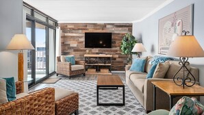 Un salon moderne avec un téléviseur à écran plat, des meubles en osier, un tapis à motifs et une grande fenêtre.