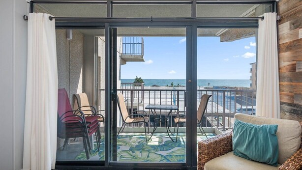 Un balcon avec vue sur l’océan, une chaise en osier avec un coussin et une table avec des chaises.