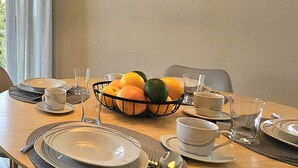 A dining table set with plates, bowls, and glasses, a fruit basket, and a painting on the wall. - Apartament Luxe w Kołobrzegu - 365PAM (Kolobrzeg)