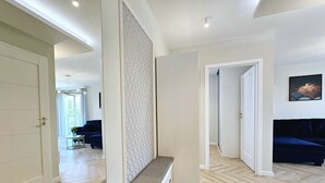 A modern interior with a hallway leading to a living area, featuring a patterned wall, a bench, and a dark blue sofa. - Apartament Luxe w Kołobrzegu - 365PAM (Kolobrzeg)