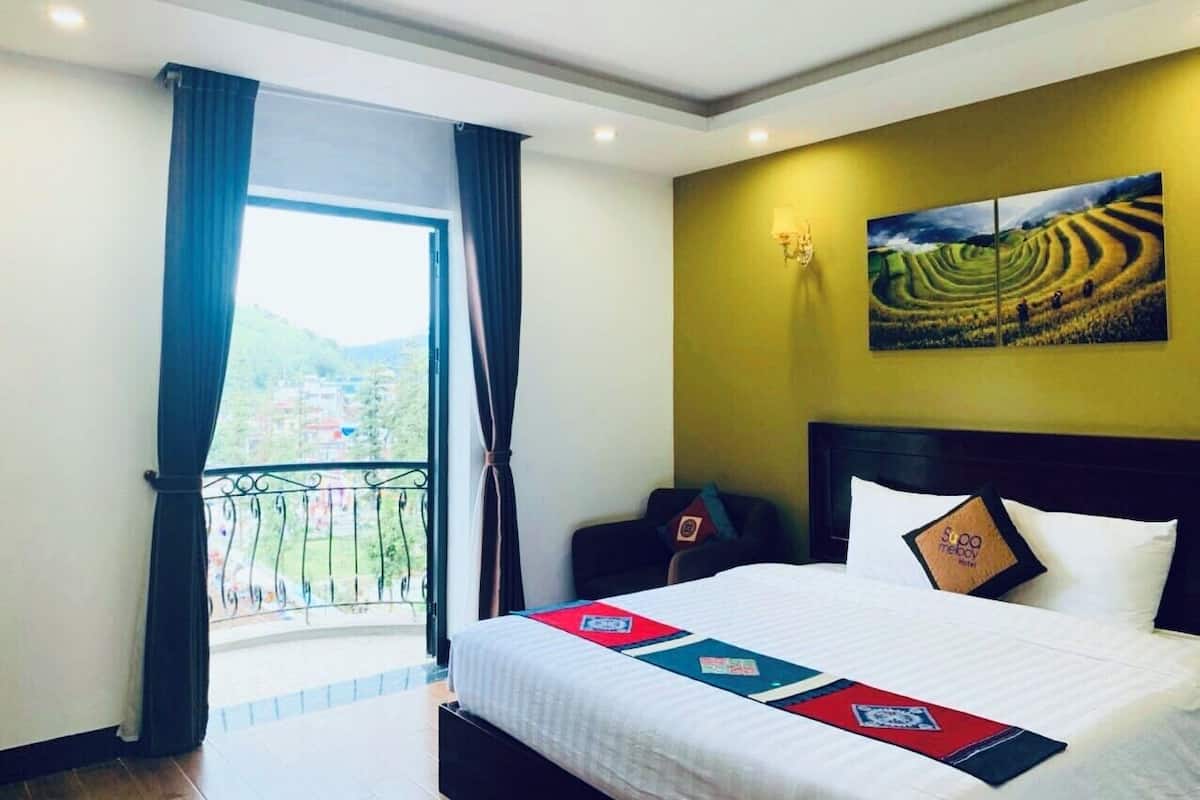 Una habitación de hotel con una cama, un cuadro en la pared y un balcón con cortinas.