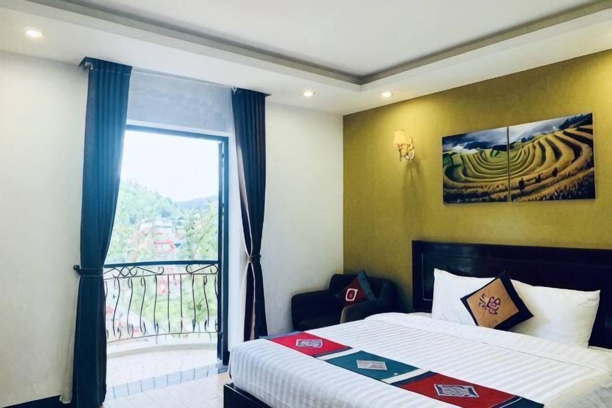 Habitación de hotel con cama, vistas al exterior, un cuadro en la pared y balcón con cortinas.