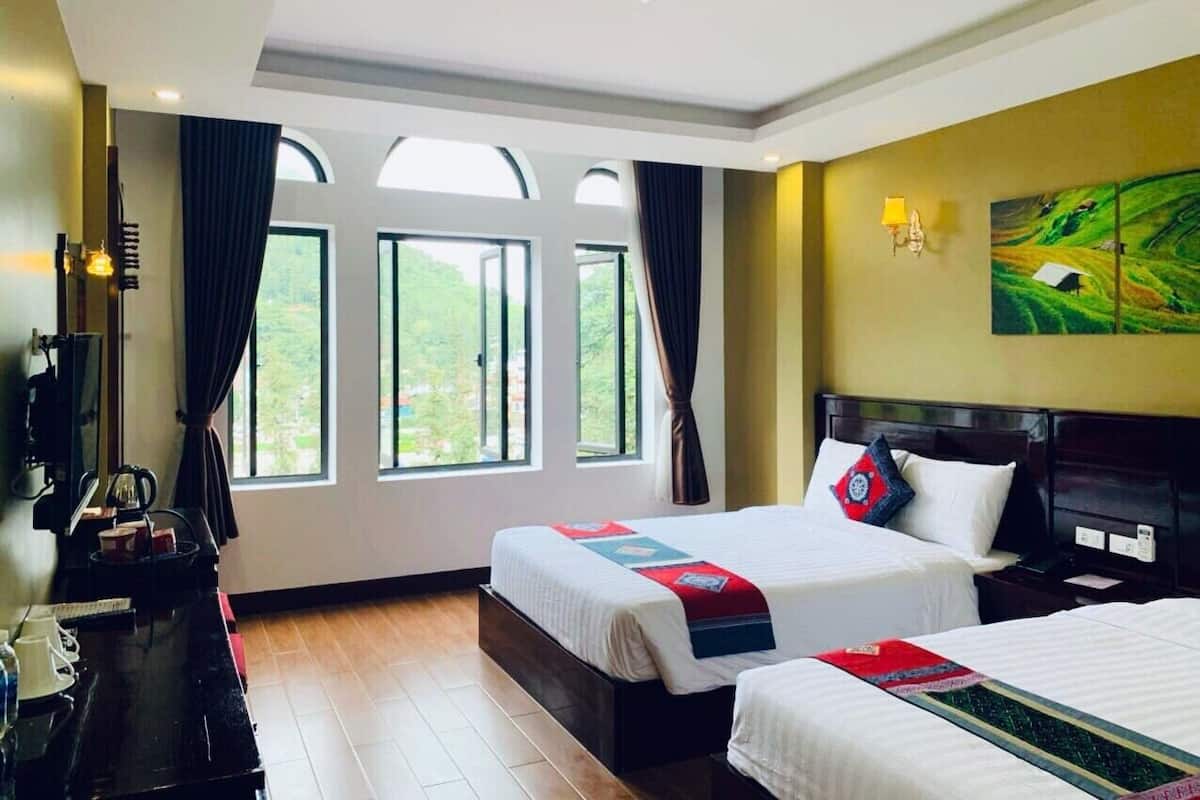 Habitación de hotel con dos camas, un escritorio con lámpara, un televisor y un cuadro en la pared.