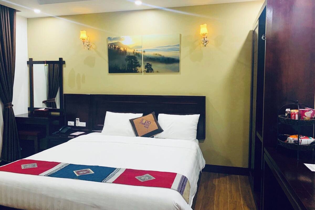 Habitación de hotel con cama, mesita de noche, espejo y lámpara de pared.