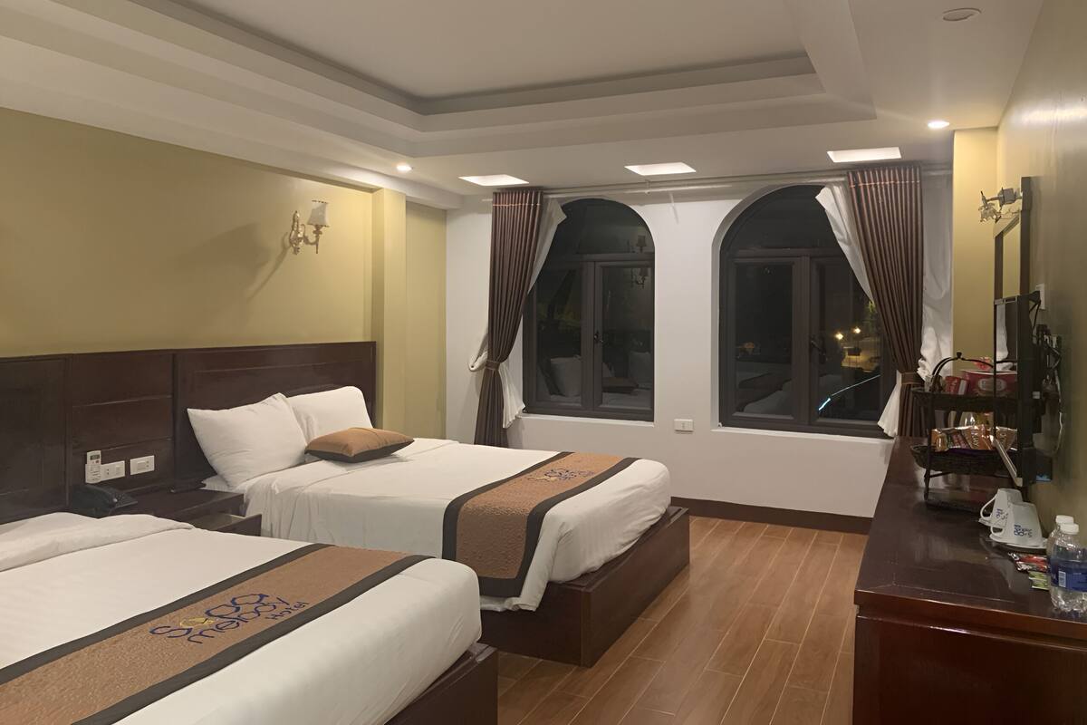 Habitación de hotel con dos camas, un cabecero de madera, un escritorio con espejo y una ventana con cortinas.