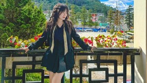 Una persona de pie en un balcón con vistas a montañas y un paisaje urbano.