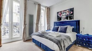 A bedroom with a large bed, a blue headboard, and a painting on the wall. - AN AUTHENTIC PARISIAN ELEGANCE MOMENTS FROM ICONIC LANDMARKS – CHAMPS ELYSEES (Paris)