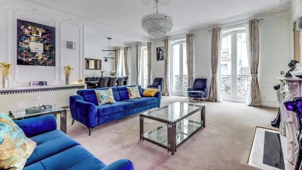A spacious living room with a blue sofa, a glass coffee table, and a chandelier. - AN AUTHENTIC PARISIAN ELEGANCE MOMENTS FROM ICONIC LANDMARKS – CHAMPS ELYSEES (Paris)