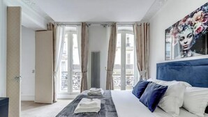 A bedroom with a bed, a radiator, and a balcony view. - AN AUTHENTIC PARISIAN ELEGANCE MOMENTS FROM ICONIC LANDMARKS – CHAMPS ELYSEES (Paris)