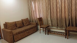 A living room with a brown sofa, a wooden chair, and a glass coffee table. - Divine Residency (Panvel)