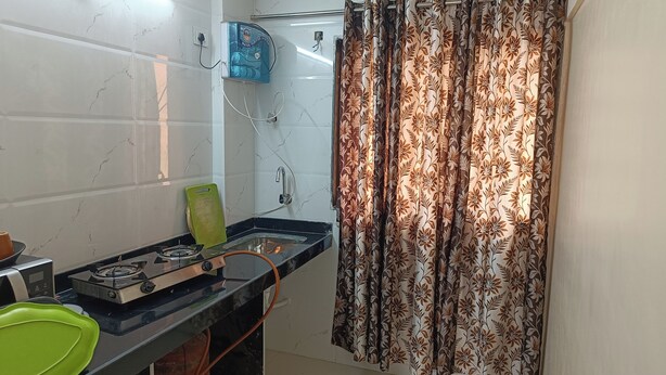 A kitchen with a gas stove, a water purifier, and a patterned curtain. - Divine Residency (Panvel)