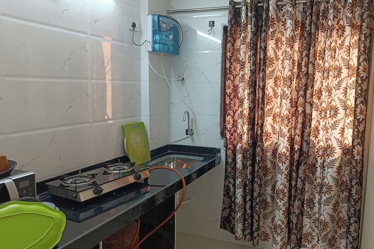 A kitchen with a gas stove, a water purifier, and a patterned curtain.