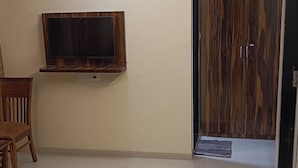 A spacious living area with a flat-screen TV mounted on a wooden panel, a ceiling fan, and a door leading to another room. - Divine Residency (Panvel)