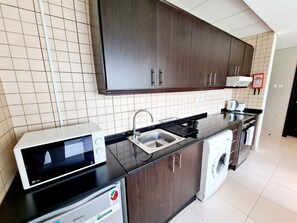Une cuisine moderne avec des meubles de couleur bois foncé, un plan de travail noir, un four à micro-ondes, un lave-linge et un évier.