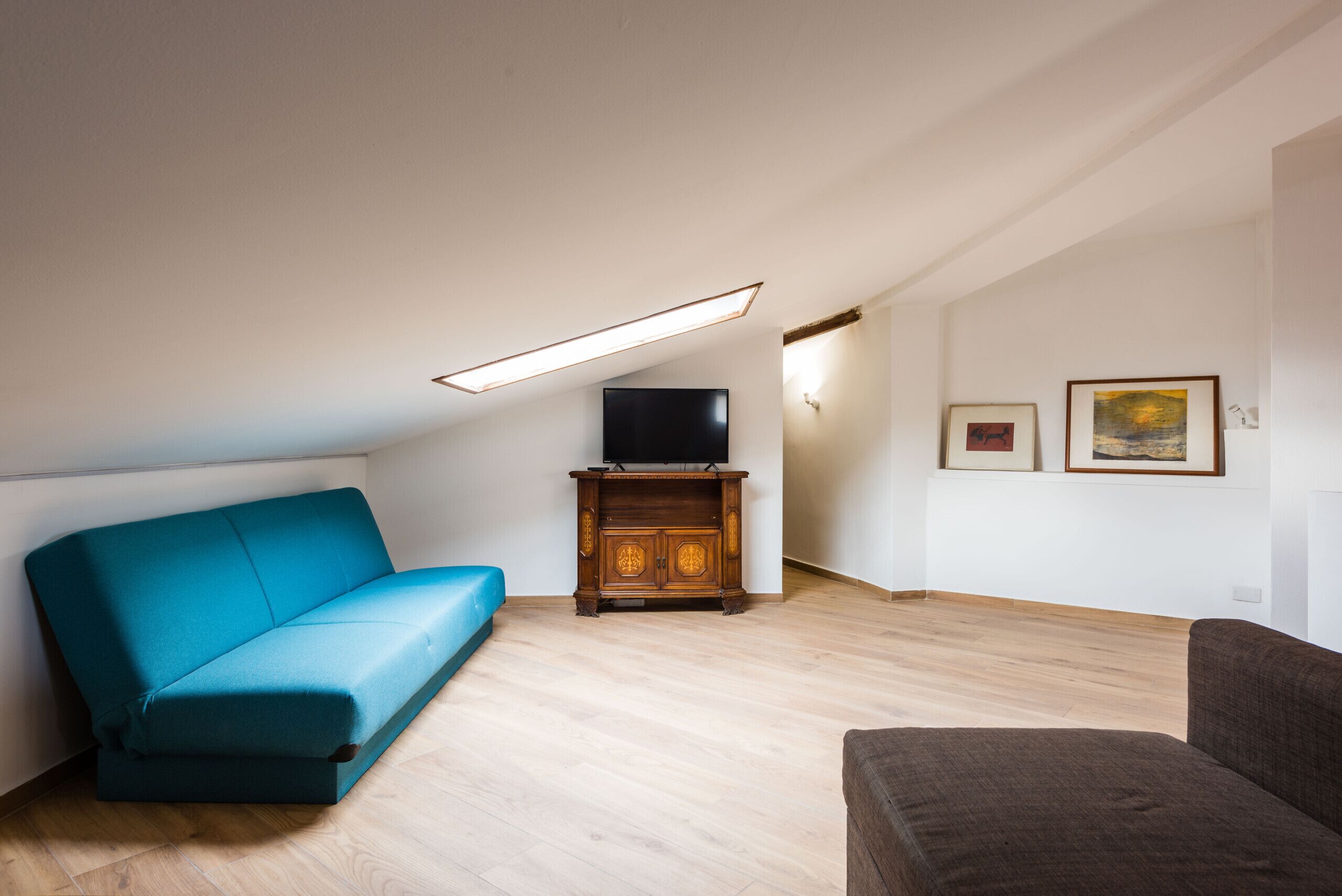 A living room with a teal sofa, a brown sofa, a wooden cabinet with a TV, and two framed pictures on the wall.