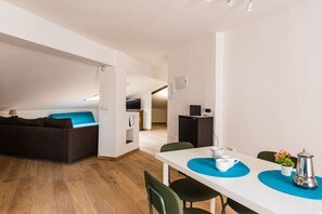 A modern, well-lit room with a white table, green chairs, a dark sofa, and a small kitchenette area. - Vulcania Loft by Wonderful Italy (Catania)