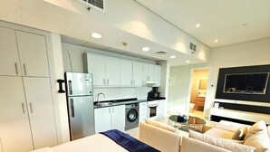 Una habitación de hotel moderna con una cama grande, un sofá, una mesa de comedor, un televisor, una zona de cocina con lavadora y un ventilador de techo.