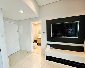 Une chambre d’hôtel moderne dotée d’un grand téléviseur à écran plat fixé sur un mur noir, d’une console blanche et d’une porte donnant accès à la salle de bain.