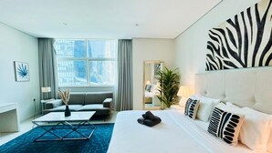 A hotel room with a large bed, a sofa, a coffee table, and a view of the city through large windows. - Sunrise Homes - Large Spacious  Studio in Business Bay (Business Bay)