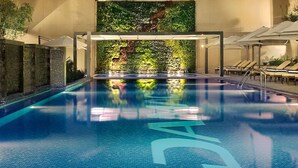 An indoor swimming pool with a tiled floor, a green wall with plants, and lounge chairs on the right side. - Sunrise Homes - Large Spacious  Studio in Business Bay (Business Bay)