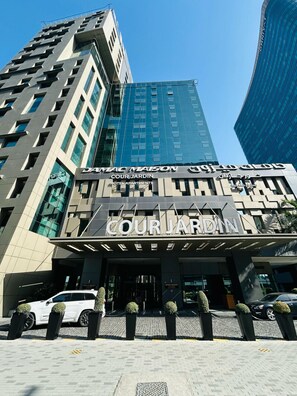 Une entrée d’hôtel moderne, avec une enseigne bien visible indiquant : « COUR JARDIN HOTEL APARTMENTS ».