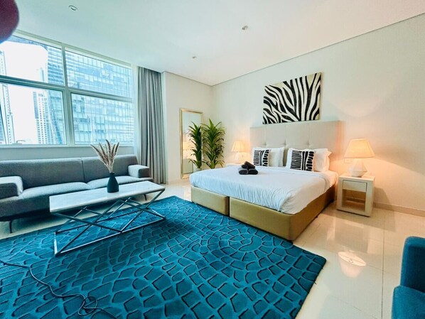 A modern hotel room with a large bed, a sofa, a coffee table, and a view of the city. - Sunrise Homes - Large Spacious  Studio in Business Bay (Business Bay)