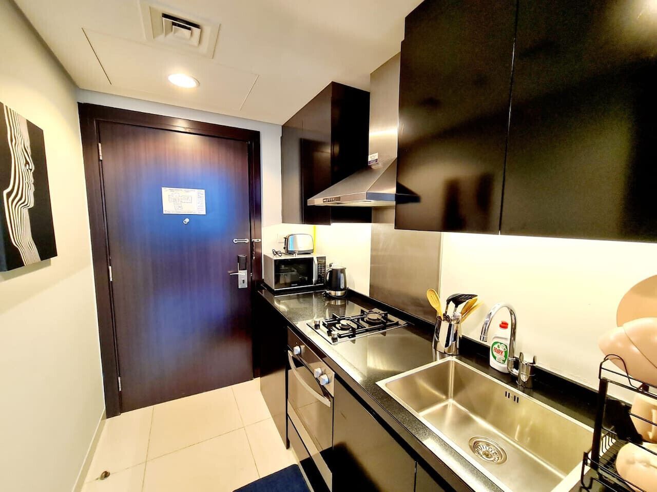 A modern kitchen with a stainless steel sink, a microwave, a stove, and a black cabinet.