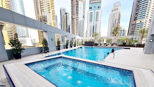 Une piscine sur le toit, avec une eau d’un bleu cristallin, entourée d’immeubles de grande hauteur et de plantes en pot.