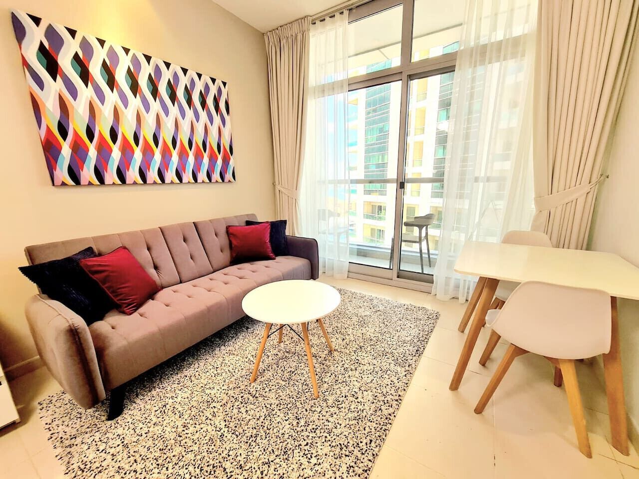 Ein modernes Wohnzimmer mit einer Couch, einem runden Couchtisch, einem Esstisch mit Stühlen und einem großen Fenster mit Vorhängen.