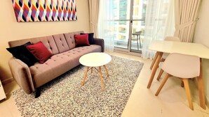 Un salon moderne comprenant un canapé, une table basse ronde, une table à manger avec des chaises et une grande fenêtre avec des rideaux.