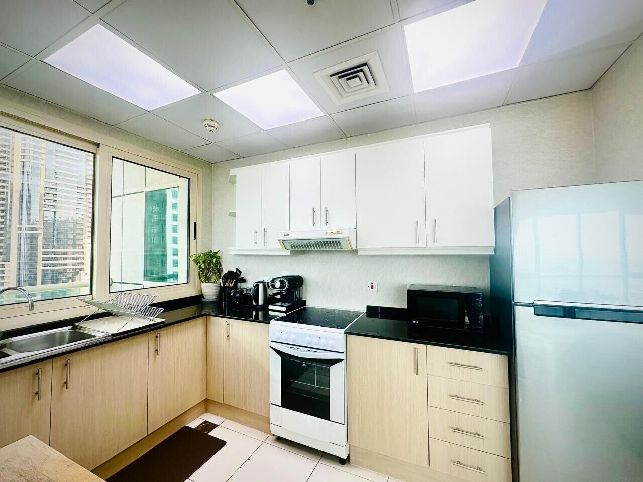 A modern kitchen with white cabinets, a stainless steel refrigerator, a stove, and a microwave.