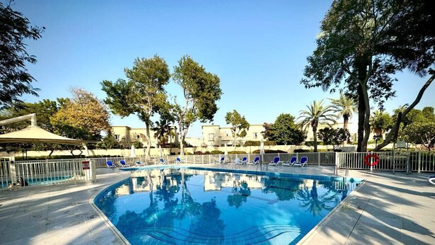 Piscina con borde de azulejos, rodeada de sillones de descanso y una valla.