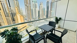 A balcony with a table and chairs, potted plants, and a view of tall buildings.