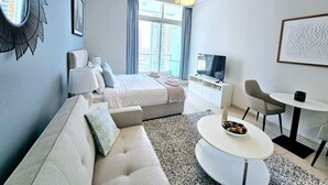 A modern hotel room with a large bed, a sofa, a dining table, and a TV.